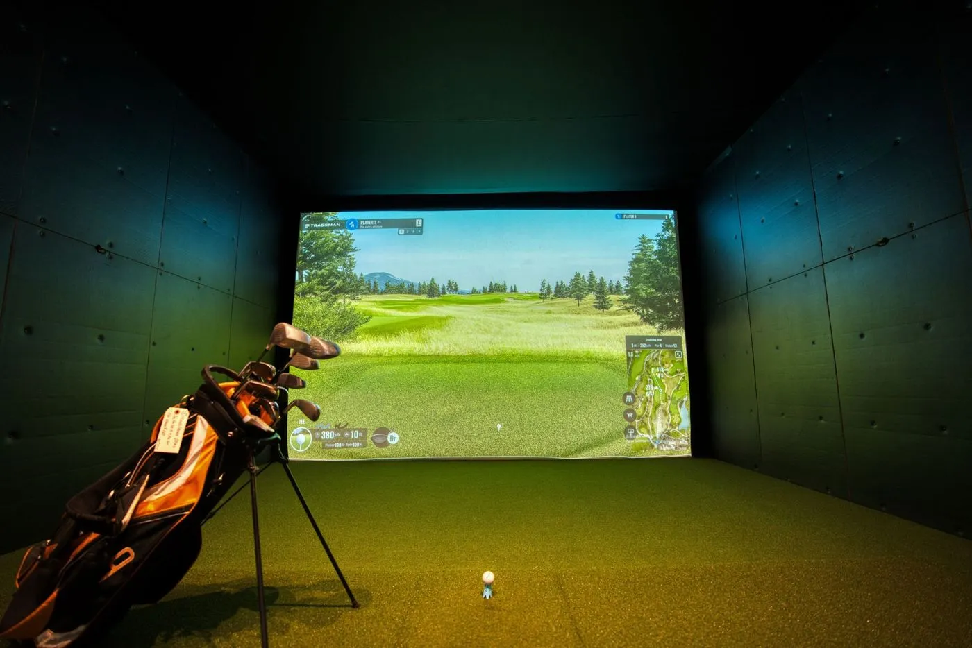 A home golf simulator hitting into a projected course on the impact screen, with clubs and turf